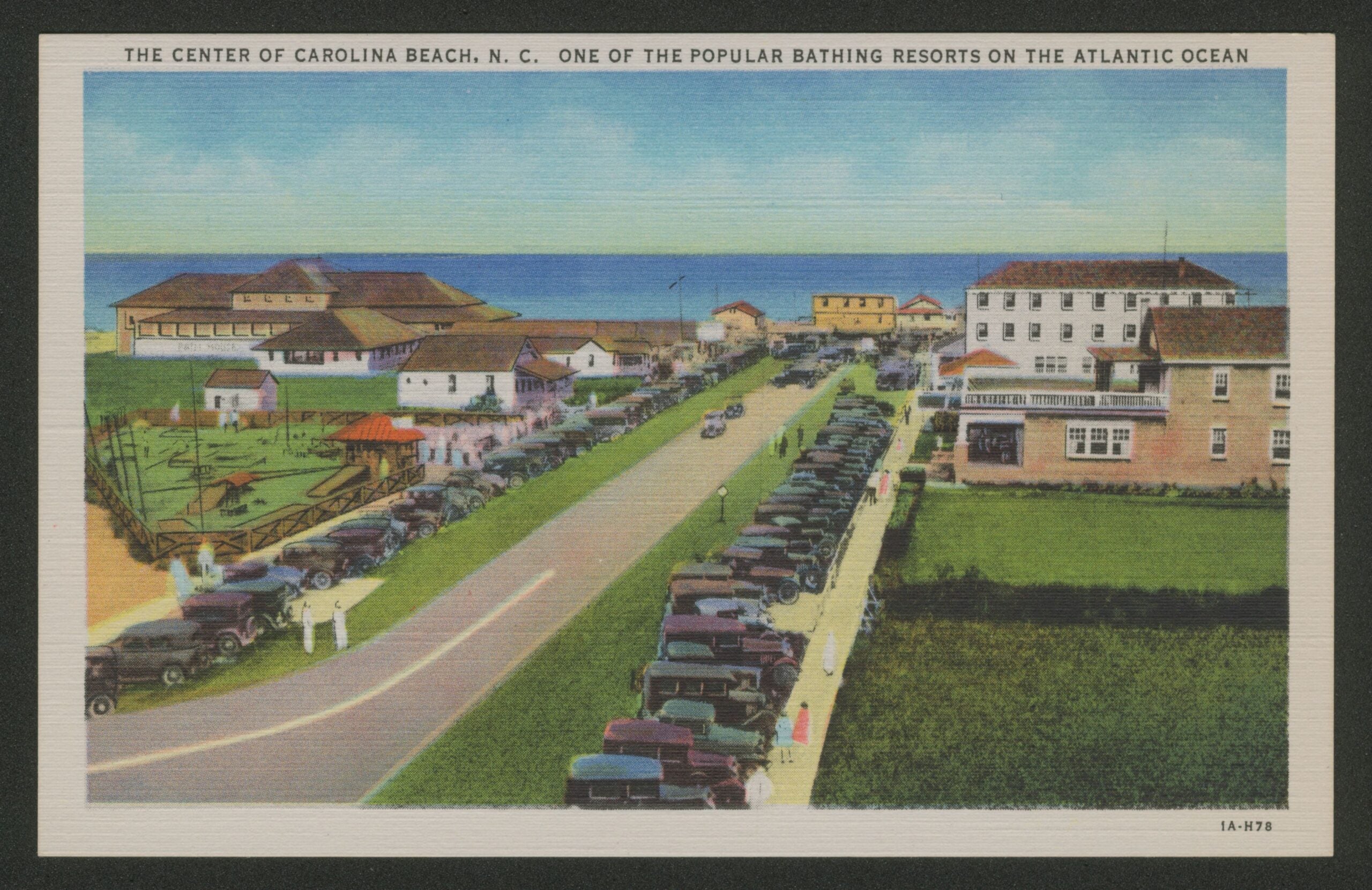 Postcard depicting a street with the ocean in the background, showing cars parked and pedestrians on the boardwalk.