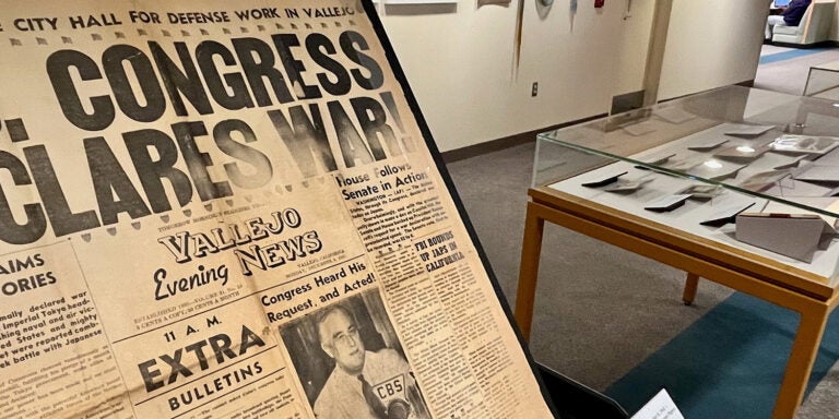 A newspaper from 1941 is displayed beside other World War II artifacts in a library.