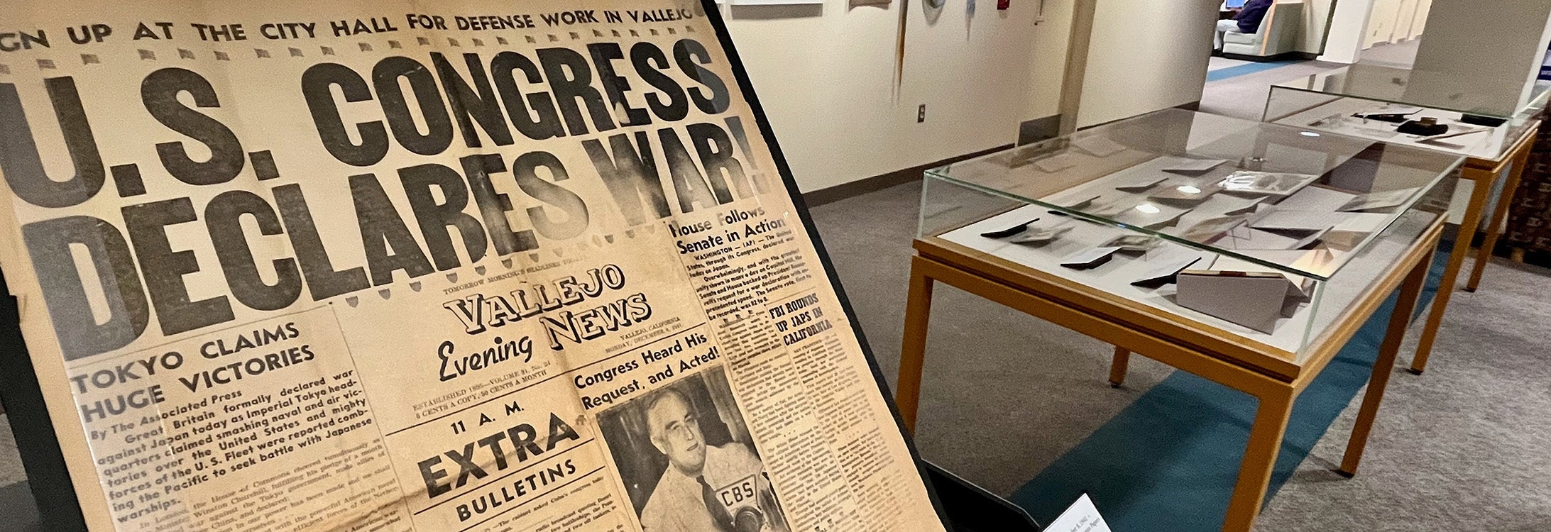 A newspaper from 1941 is displayed beside other World War II artifacts in a library.