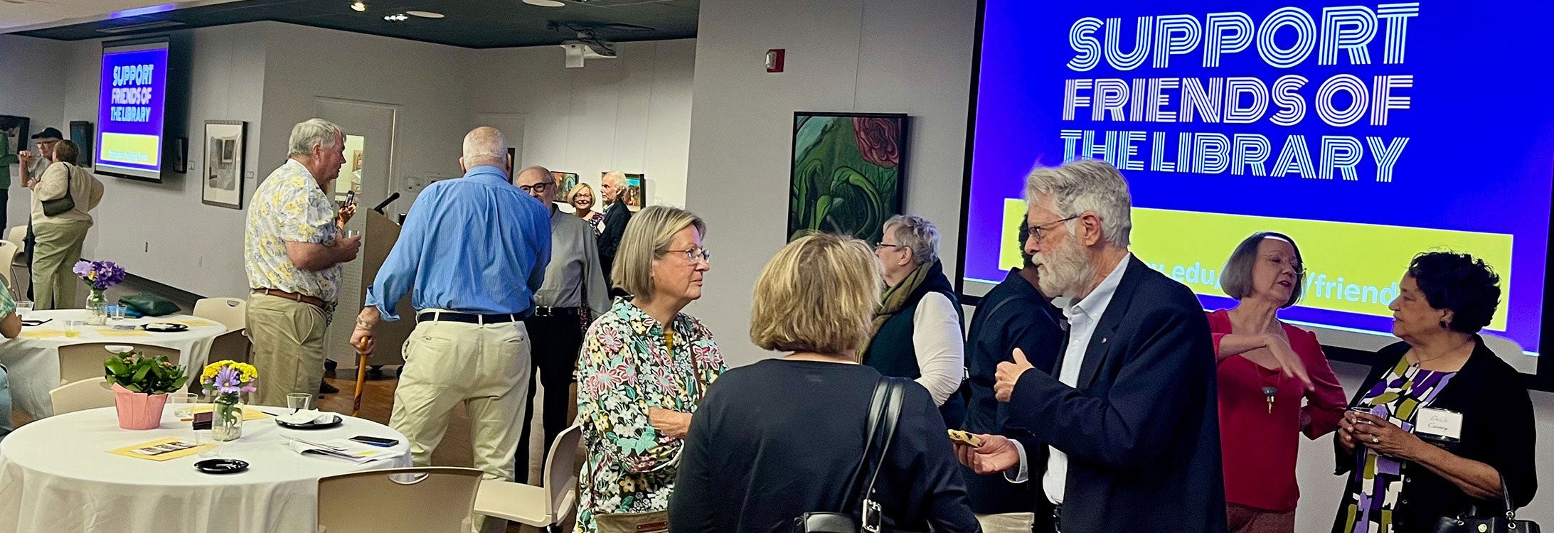People gathered and talking in a library art gallery.