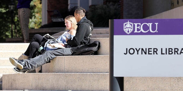 Two students sitting on steps reading outside library