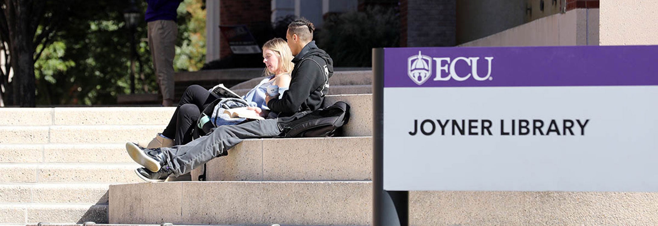 Two students sitting on steps reading outside library